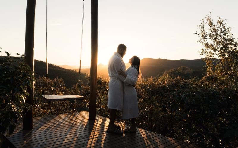 Casal no balanço suspenso da Villa Eyá contra o pôr do sol sobre o vale